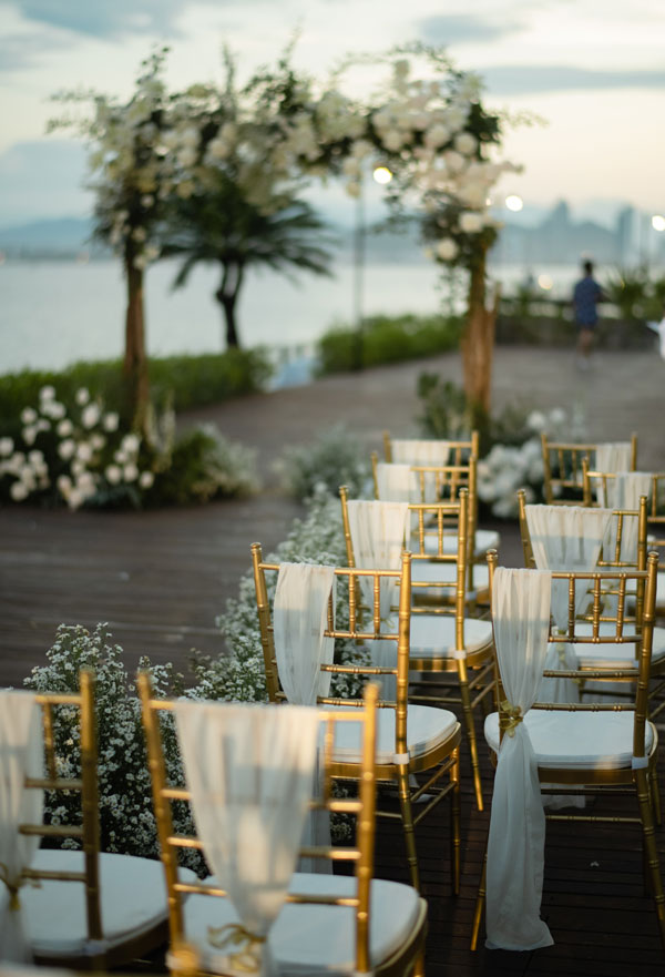 Nha Trang Wedding Resort Decor: Amiana and Alibu Ceremonies Gold Chiavari chairs tied with white chiffon along the aisle, timber arch and city skyline
