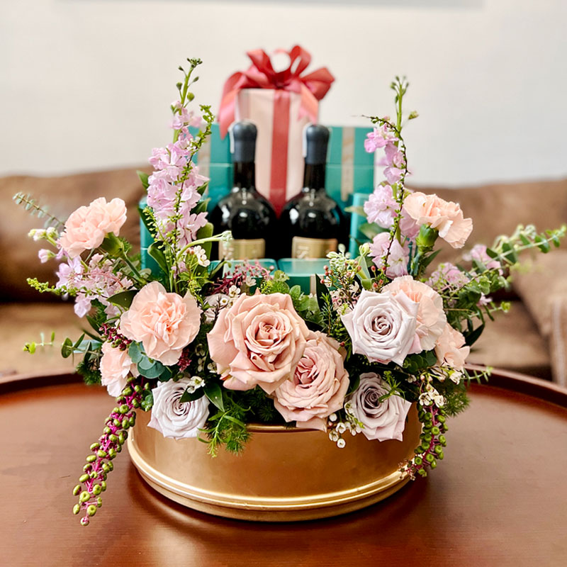 Mâm Quả Cưới Nha Trang, Tráp Ăn Hỏi Từ 2,5 Triệu Mâm rượu và hộp quà đỏ giữa hoa hồng phấn, hoa trắng và cành hoa tím trên khay tròn vàng