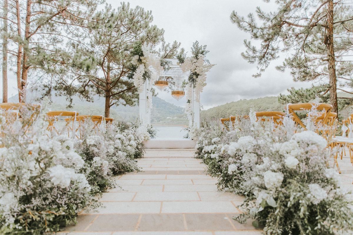 White flower aisle on pale paving leading to a white arch, lake and hills behind White flower aisle on pale paving leading to a white arch, lake and hills behind