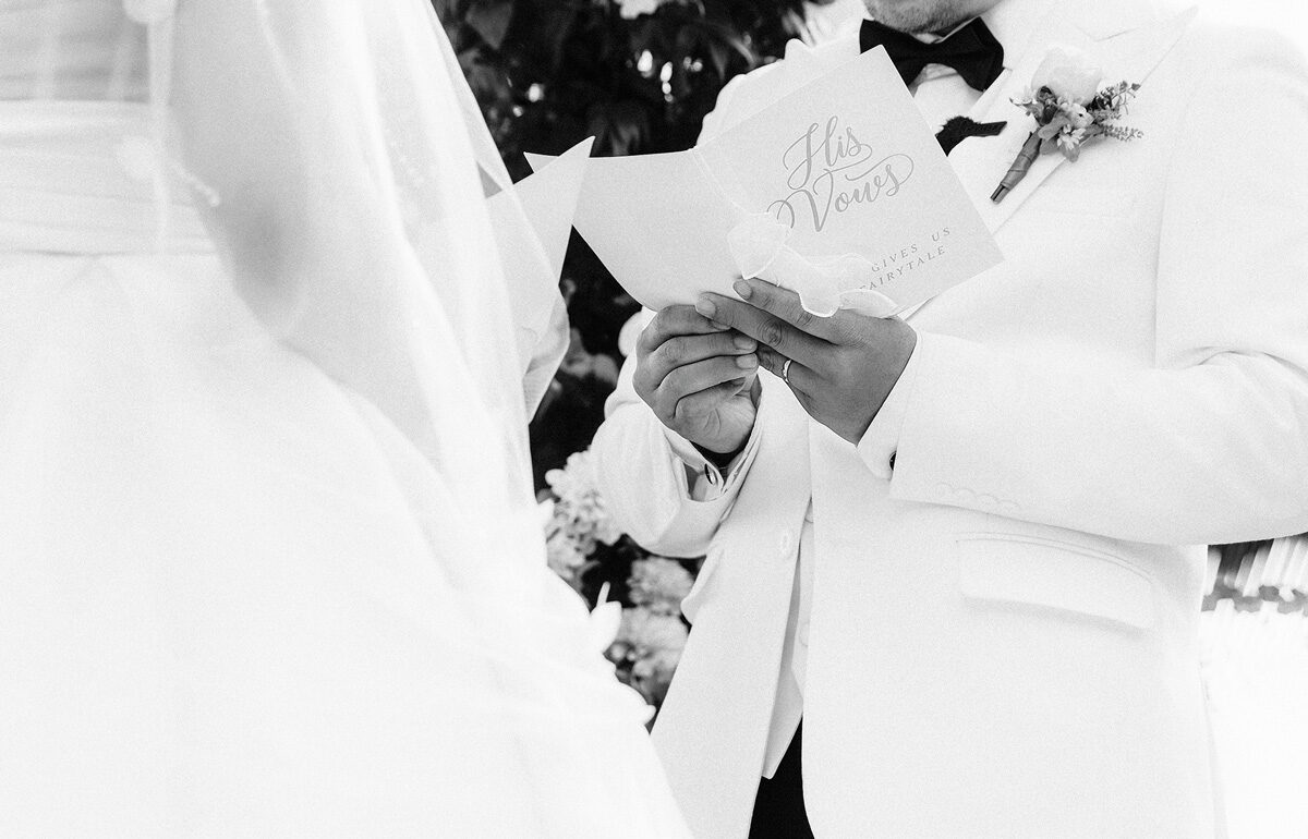 Groom in a white jacket holding his vow card, black and white photo Groom in a white jacket holding his vow card, black and white photo