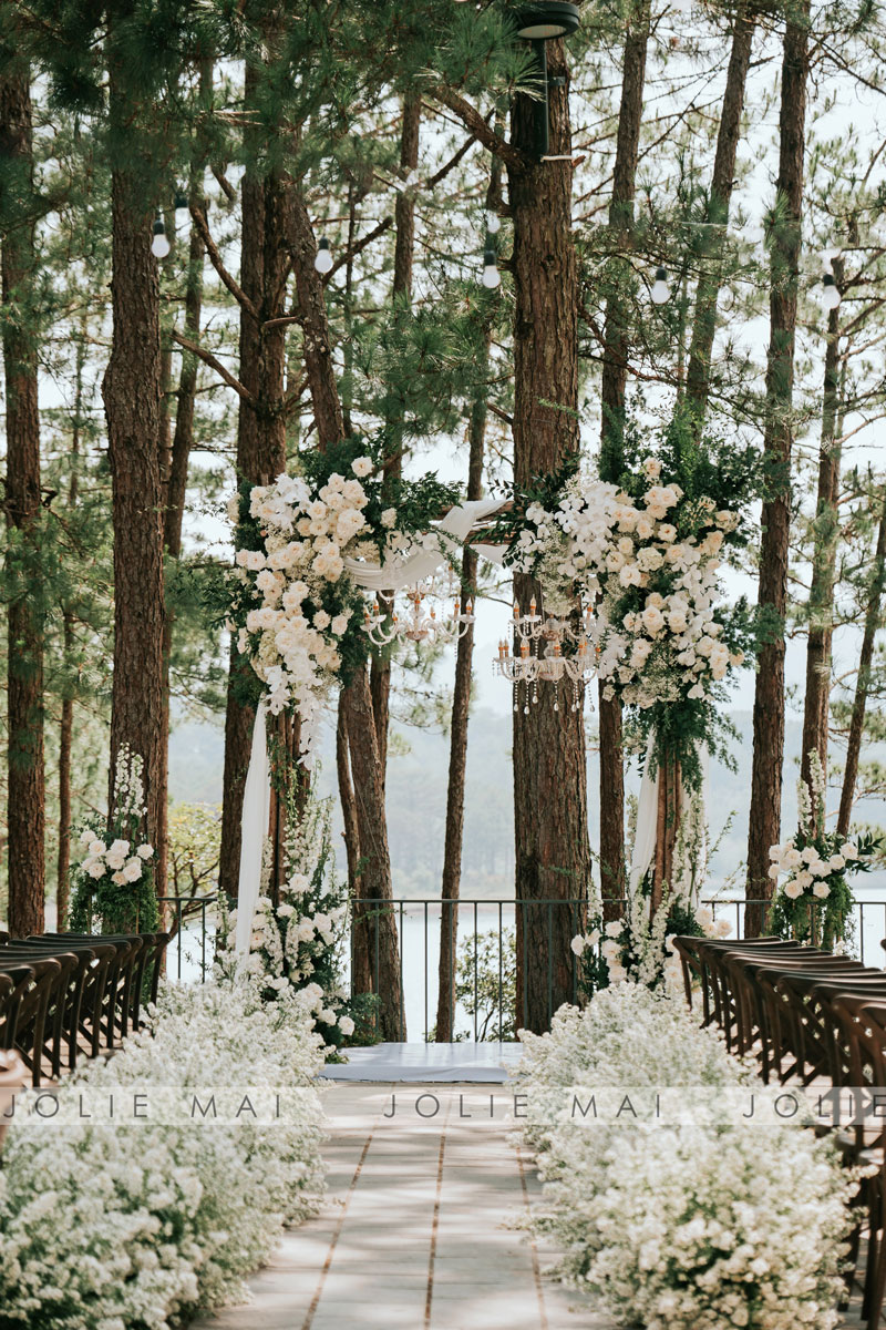 Stone-paved aisle lined with low white flowers leading to the arch under the pines Stone-paved aisle lined with low white flowers leading to the arch under the pines