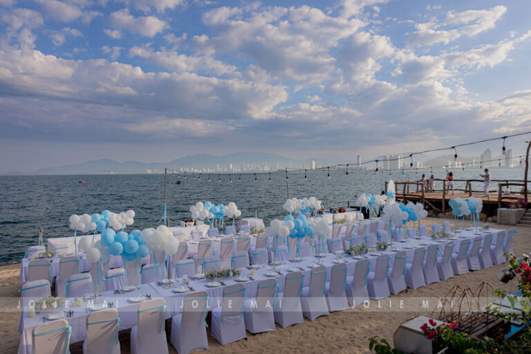 Trang Trí Sinh Nhật Nha Trang: Bãi Biển, Resort, Tại Nhà Trang trí sinh nhật Nha Trang: hàng bàn tiệc dài trên bãi cát lúc hoàng hôn, trụ bóng bay xanh trắng