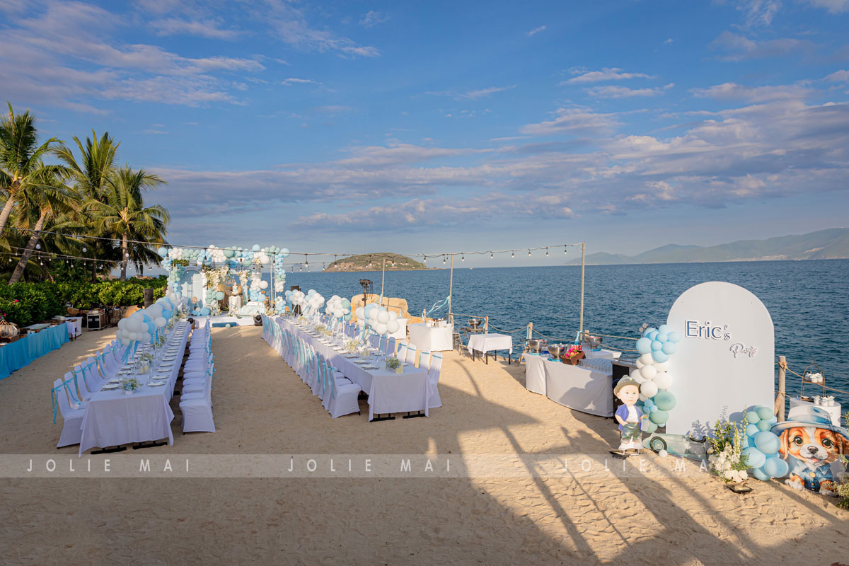 Trang Trí Sinh Nhật Nha Trang: Bãi Biển, Resort, Tại Nhà Trang trí sinh nhật Nha Trang tiệc bé trai trên cát: hai dãy bàn trắng, vòm trắng chữ Eric's Party phía xa