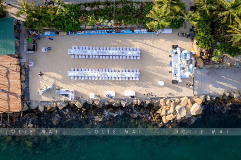 Trang Trí Sinh Nhật Nha Trang: Bãi Biển, Resort, Tại Nhà Toàn cảnh hai dãy bàn tiệc sinh nhật trên dải cát hẹp nhìn thẳng từ trên cao, sát bờ đá và biển