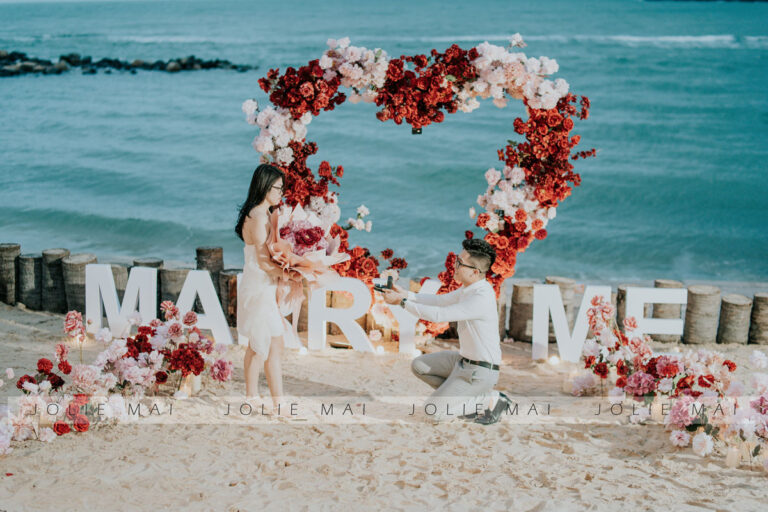 Trang Trí Tiệc Nha Trang: Sinh Nhật, Kỷ Niệm, Tất Niên Và Giáng Sinh Chú rể quỳ gối trước vòng hoa trái tim và chữ MARRY ME bên bờ biển Nha Trang