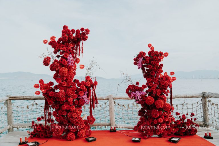 Trang Trí Tiệc Nha Trang: Sinh Nhật, Kỷ Niệm, Tất Niên Và Giáng Sinh Hai cột hoa hồng đỏ cao trên thảm đỏ ở sàn gỗ ven biển trong tiệc kỷ niệm ngày cưới