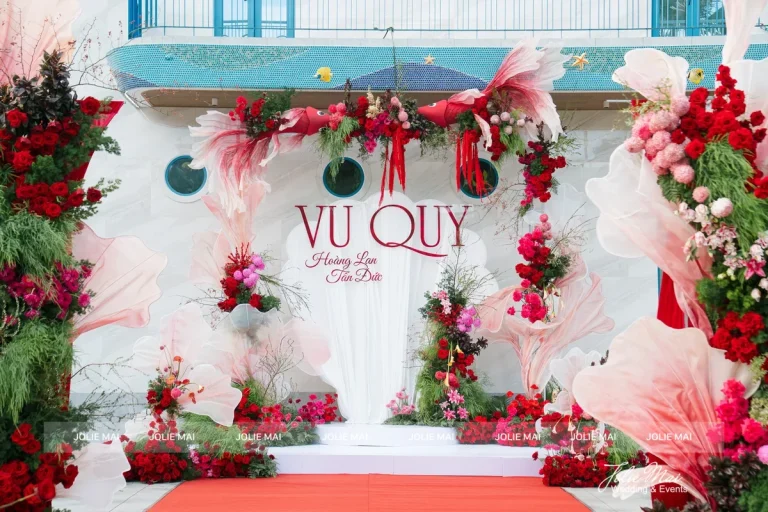 Dịch Vụ Cưới Nha Trang Một Đầu Mối: Gia Tiên, Tiệc, Mâm Quả Cổng vu quy hoa đỏ, hồng và cánh hoa vải hồng phấn, thảm đỏ dọc lối vào nhà