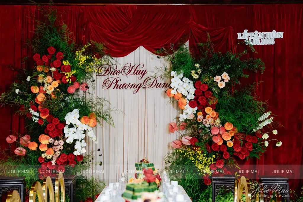 Jolie Mai Wedding: 12 năm trang trí tiệc cưới tại Nha Trang Bàn lễ gia tiên phông voan kem, rèm nhung đỏ, hoa đỏ cam do Jolie Mai Wedding trang trí