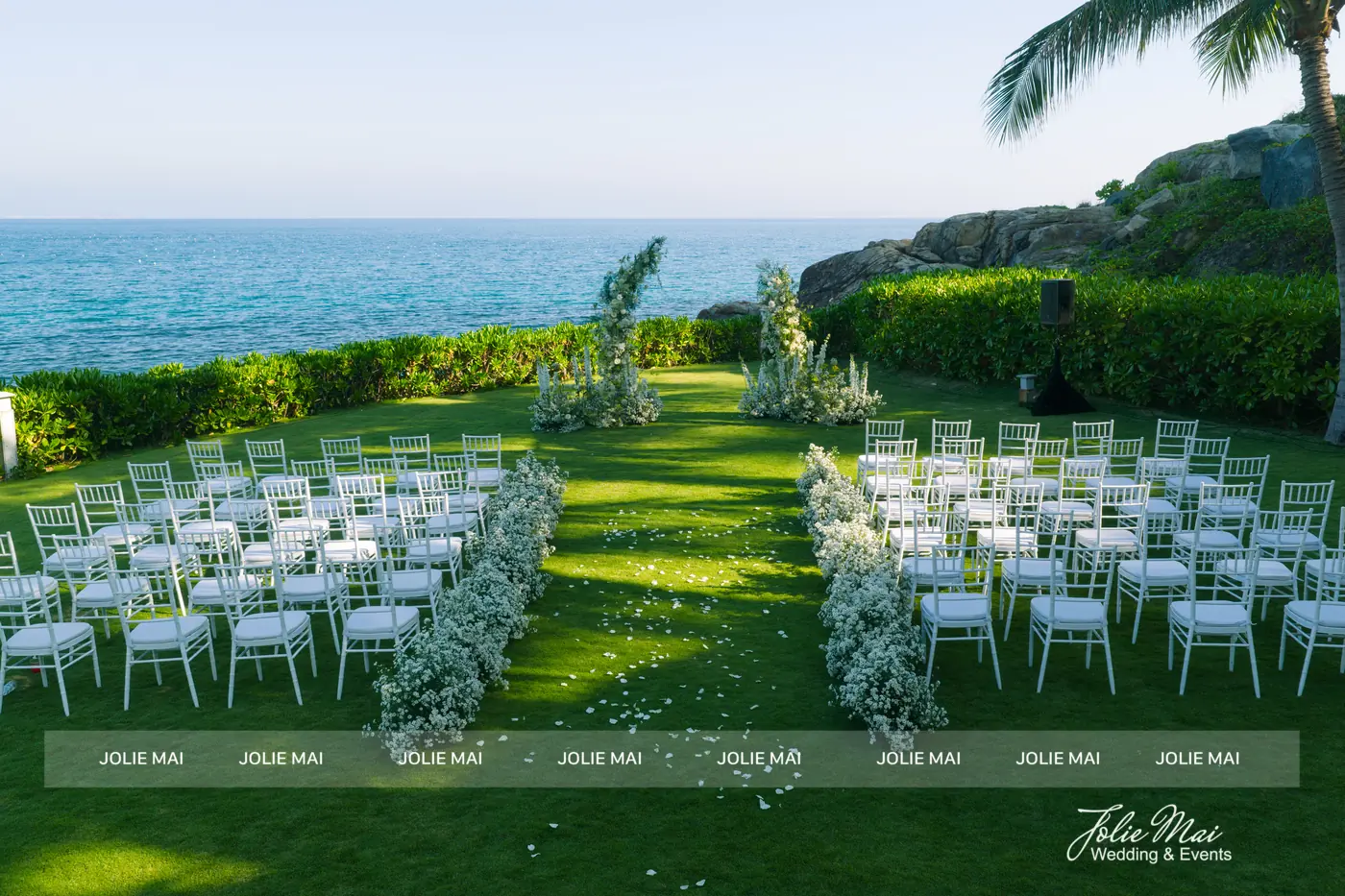 Dịch Vụ Cưới Nha Trang Một Đầu Mối: Gia Tiên, Tiệc, Mâm Quả Khu lễ trên bãi cỏ sát biển: hai khối ghế Tiffany trắng đối xứng, hai dải hoa trắng dọc lối đi ra phía biển
