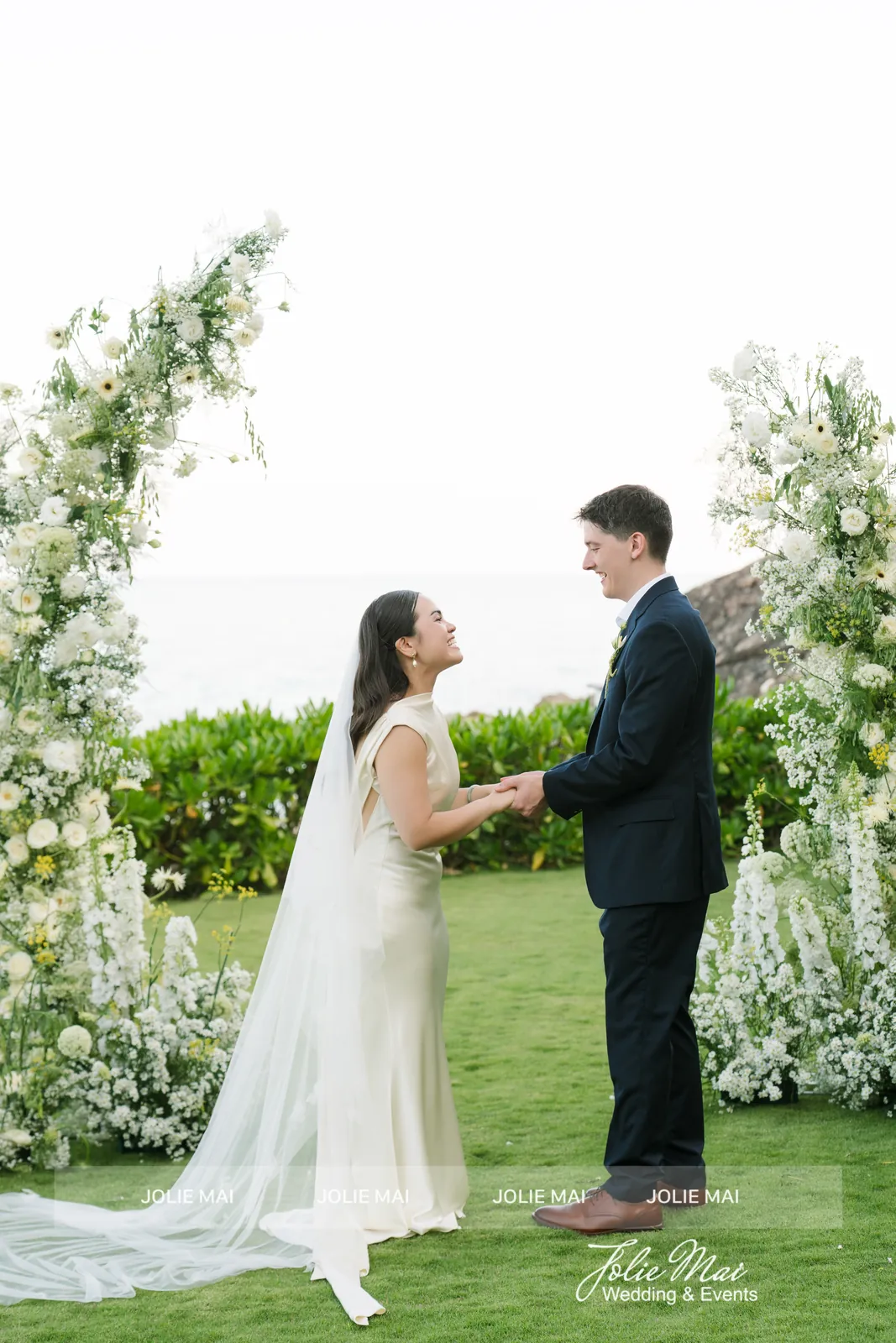 Couple holding hands for their vows between white flower pillars on the lawn at Mia Resort Nha Trang Couple holding hands for their vows between white flower pillars on the lawn at Mia Resort Nha Trang