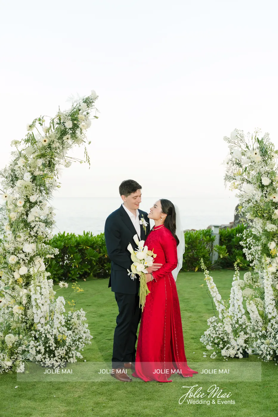 Bride in a red ao dai with white lilies beside the groom between two white flower pillars at Mia Resort Nha Trang Bride in a red ao dai with white lilies beside the groom between two white flower pillars at Mia Resort Nha Trang