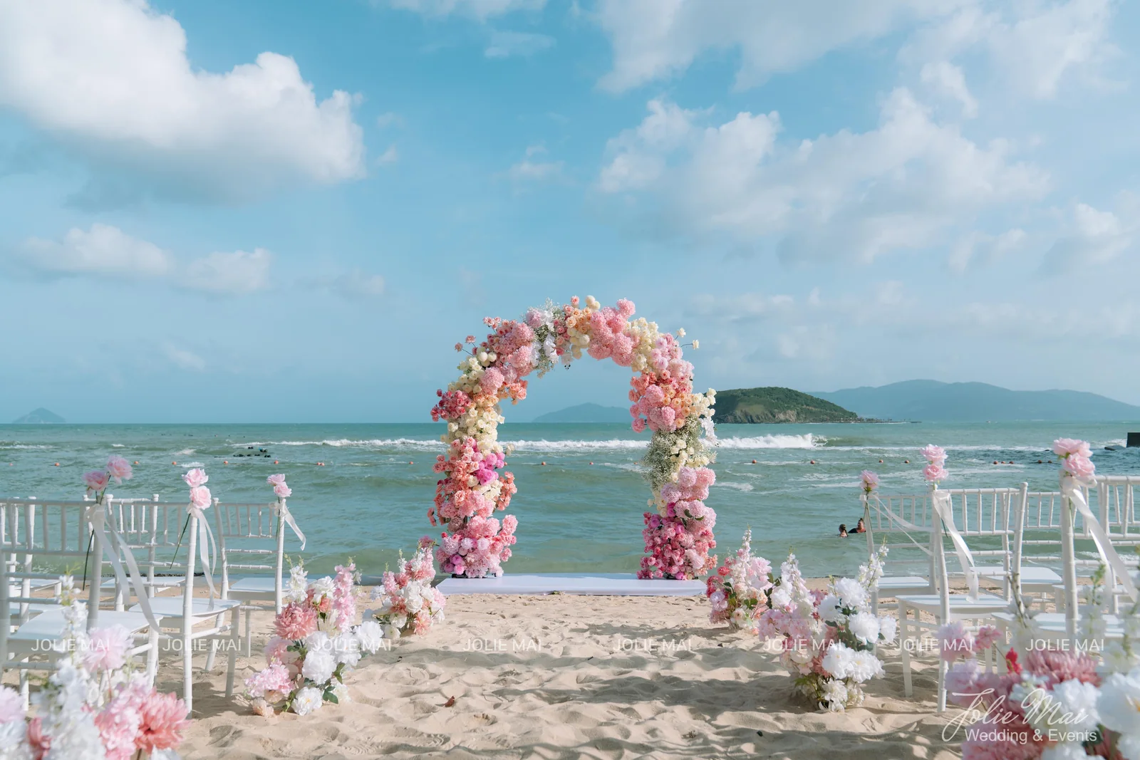 Wedding planner Nha Trang: pink and cream flower arch on the beach at Vega City with white chairs facing the sea Wedding planner Nha Trang: pink and cream flower arch on the beach at Vega City with white chairs facing the sea