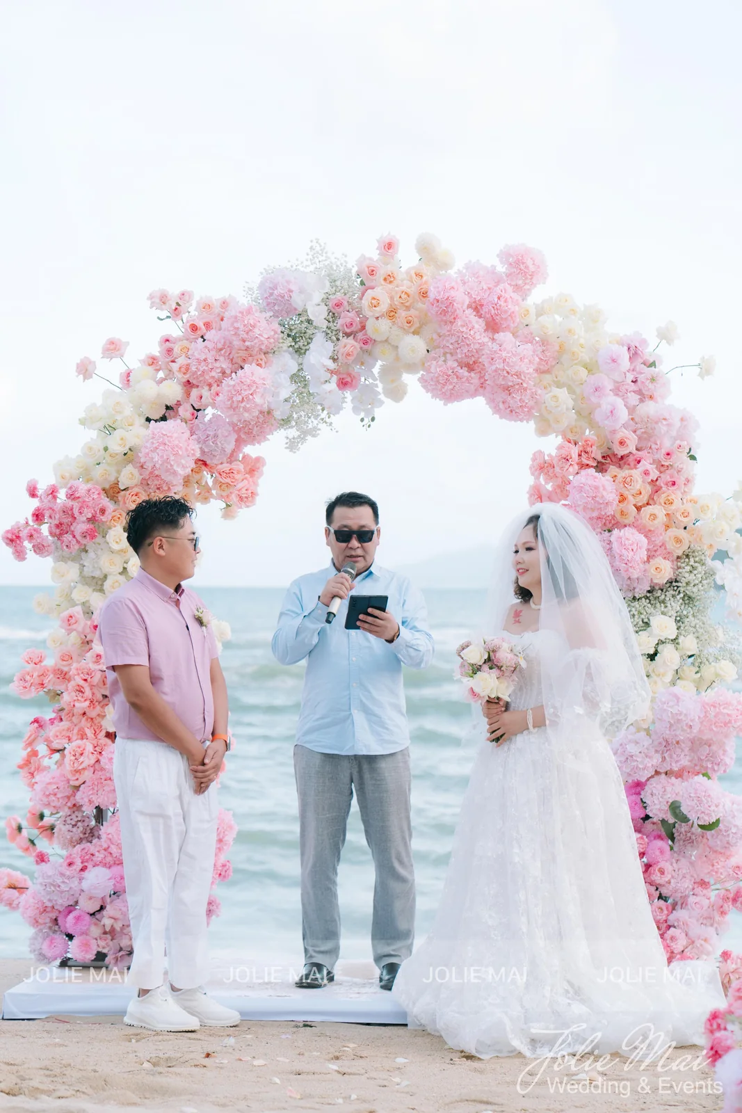 Mongolian groom reading his vows into a microphone under a flower arch at a Vega City beach wedding Mongolian groom reading his vows into a microphone under a flower arch at a Vega City beach wedding