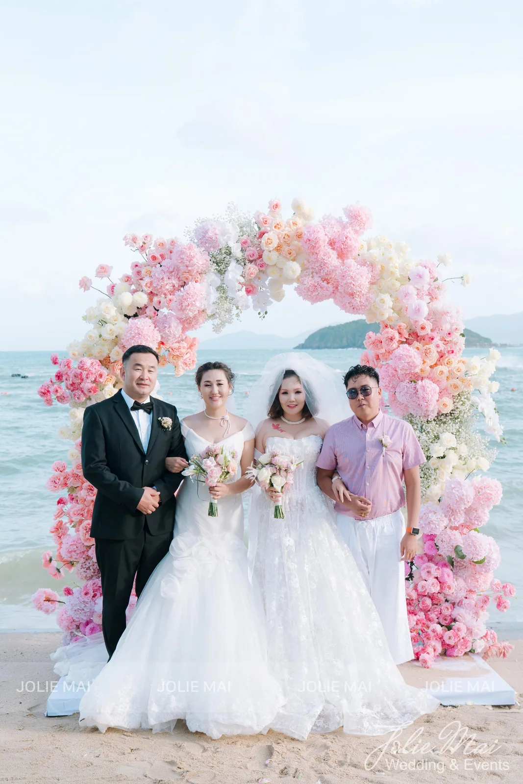 Two Mongolian couples who married together, posing with bouquets in front of the beach flower arch Two Mongolian couples who married together, posing with bouquets in front of the beach flower arch