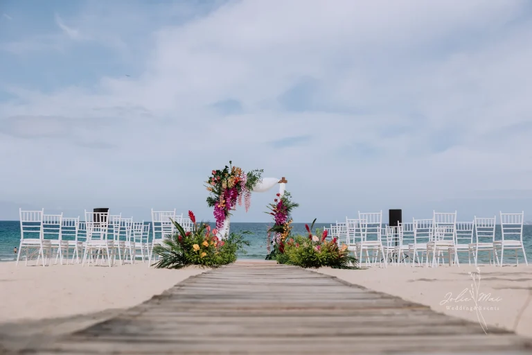 Quay Chụp Phóng Sự Cưới Nha Trang: Một Đầu Mối Từ Trang Trí Đến Thước Phim Lối đi ván gỗ trên cát dẫn tới cổng hoa ở cuối, hai khối ghế trắng hai bên và biển phía sau
