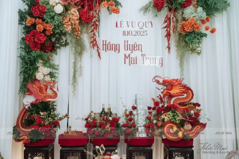 Trang Trí Gia Tiên Nha Trang: Hoa Lụa Từ 9,8 Triệu Bàn lễ bốn bục nhung đỏ dưới phông voan trắng chữ Lễ Vu Quy, hai bên là rồng đỏ cam tạo hình và hoa đỏ