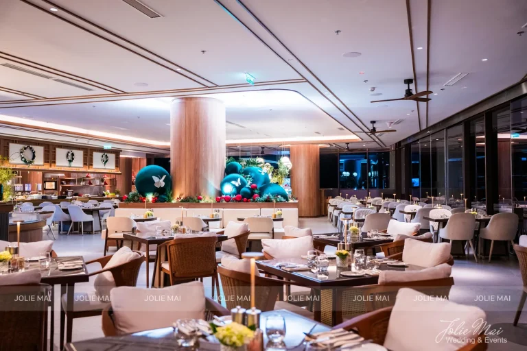 Trang Trí Tiệc Nha Trang: Sinh Nhật, Kỷ Niệm, Tất Niên Và Giáng Sinh Nhà hàng khách sạn buổi tối với bàn tiệc, nến, hoa vàng và cụm quả cầu nhung xanh ngọc phía xa