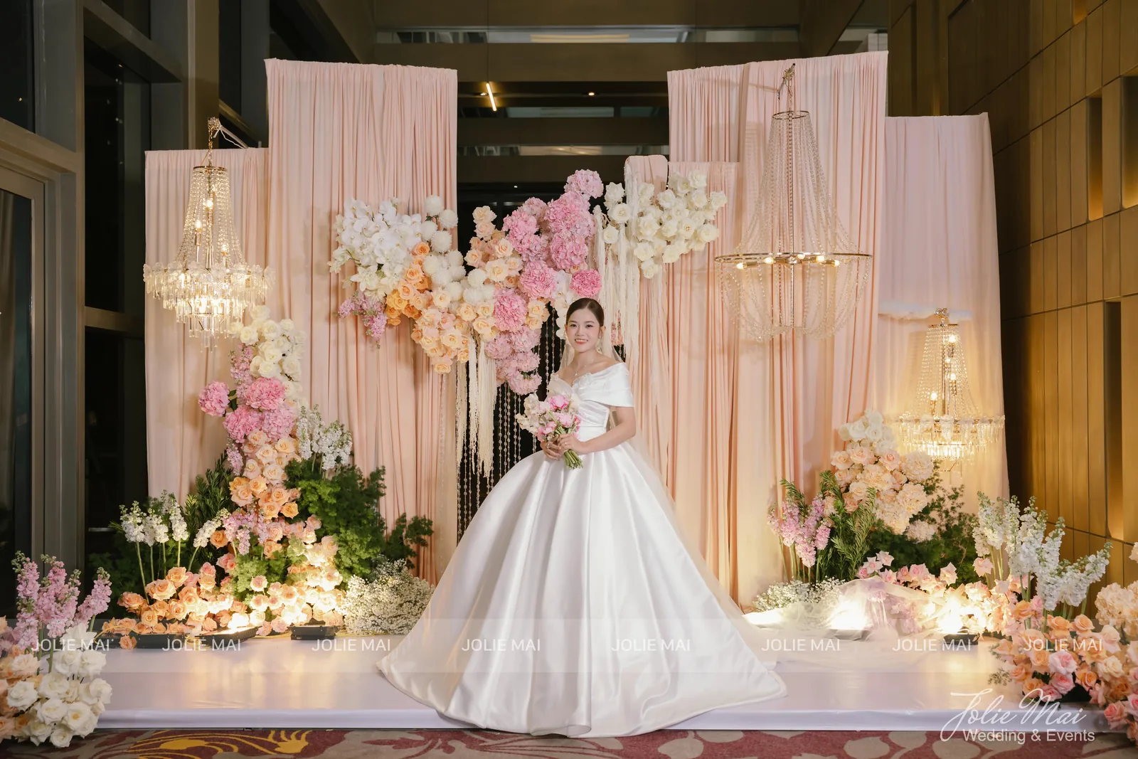 Dịch Vụ Cưới Nha Trang Một Đầu Mối: Gia Tiên, Tiệc, Mâm Quả Dịch vụ cưới Nha Trang tại InterContinental Nha Trang: cô dâu trước sân khấu rèm voan đào, đèn chùm pha lê và mảng hoa hồng phấn