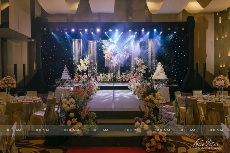 Dịch Vụ Cưới Nha Trang Một Đầu Mối: Gia Tiên, Tiệc, Mâm Quả Sảnh tiệc nhìn dọc lối đi: sân khấu nền sao với rèm pha lê, hoa thấp hai bên lối và bàn khách hai bên